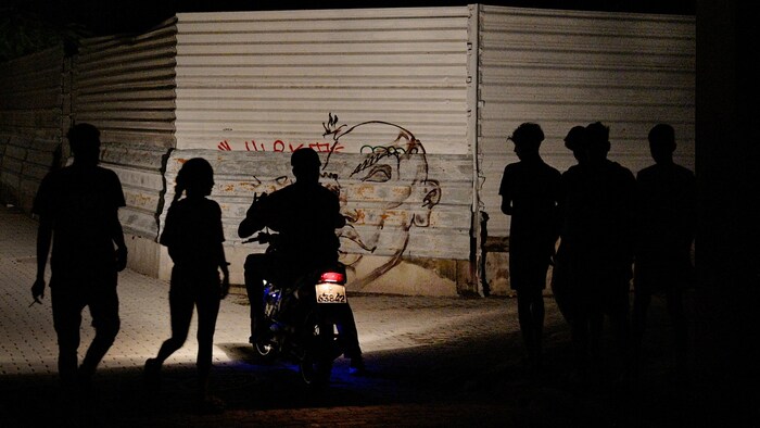 A dark street in Havana is lit only by the headlight of a moped.
