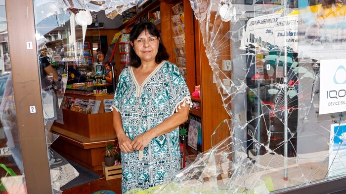 Tobacconist Angelika Stabau shows the destroyed shop window