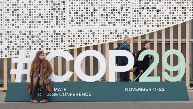 Eine Teilnehmerin sitzt auf einem Schild zur UN-Klimakonferrenz in Baku. (Bild: ASSOCIATED PRESS)