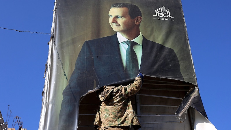 Nach Vertreibung seiner Armee demontiert ein islamistischer Rebell in Aleppo ein Plakat von Präsident Bashar al-Assad. (Bild: APA/AFP/Mohammed AL-RIFAI)