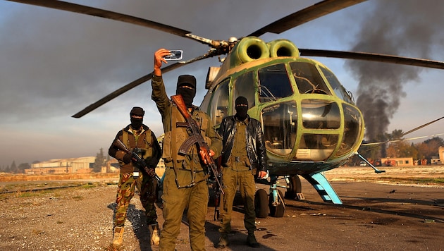 Rebels pose for a selfie in front of an army helicopter captured in Aleppo. (Bild: APA/AFP/AAREF WATAD)