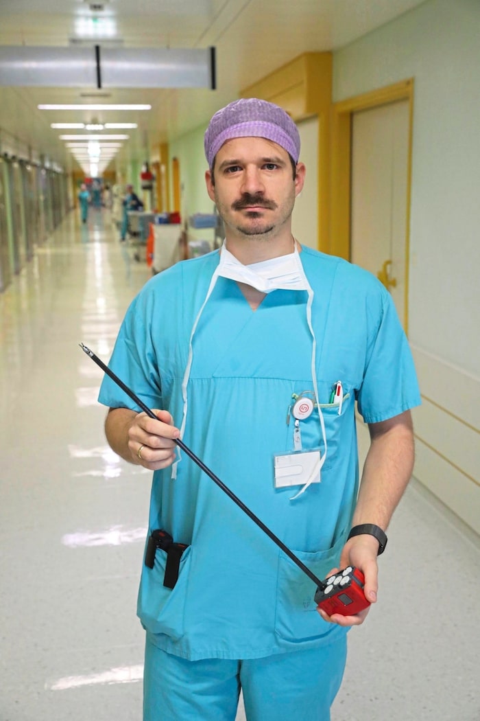 Dr. Benjamin Glaser with part of the robot that disappears into the patient. The tiny gripper ...