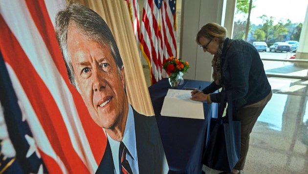 A woman writes words of remembrance in a book of condolence for Jimmy Carter. (Bild: Jeff Gritchen/The Orange County Register via AP)