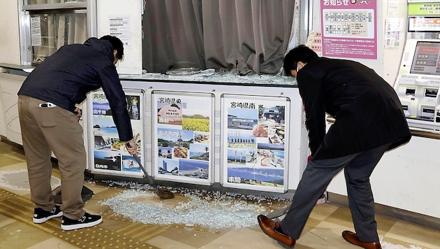 Angestellte kehren Glasscherben einer zerbrochenen Schaufensterscheibe am Flughafen von Miyazaki zusammen. (Bild: APA/AP)