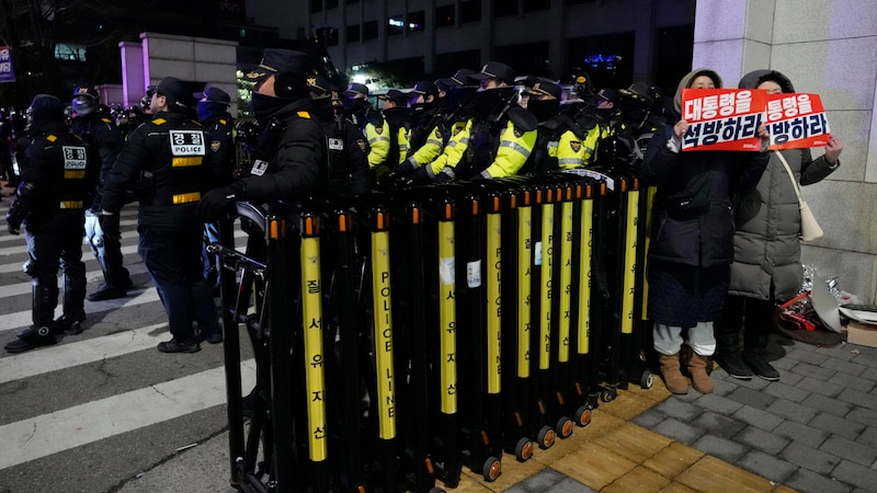 Yoons Unterstützer halten ein Schild mit der Botschaft „Lasst den Präsidenten frei“ in die Höhe. – die Exekutive sicherte inzwischen den Bereich um das Gericht ab.  (Bild: APA/Associated Press)