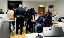 Die jungen Angeklagten werden umringt von Justizwachebeamten vorgeführt.