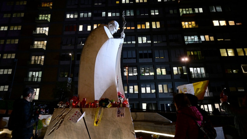 Ein nachts aufgenommenes Foto zeigt die Statue von Johannes Paul II. am Gemelli-Universitätskrankenhaus, wo Papst Franziskus behandelt wird. (Bild: Foto-/Videocredit: APA/AFP/Tiziana FABI)