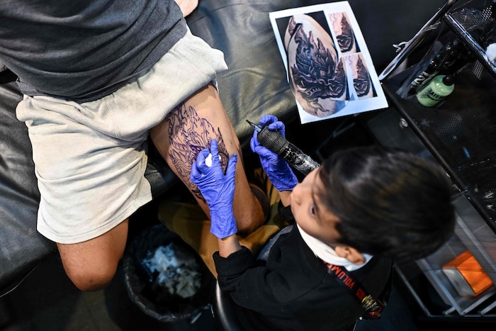 Der Neunjährige tätowiert seinem Onkel auf der Tattoomesse eine Schlange auf den Oberschenkel.