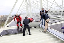 Sportstadtrat Peter Hacker (rechts hinten) und Neos-Sportsprecher Markus Ornig (re.) helfen bei der Montage des finalen Photovoltaik-Moduls am Stadiondach mit. (Bild: Jöchl Martin)