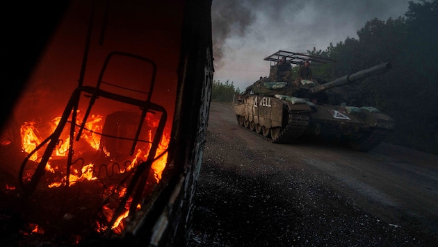 Ein ukrainischer Panzer fährt nahe der russischen Grenze an einem brennenden Fahrzeug vorbei.