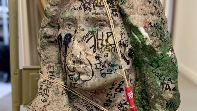 Die Skulptur aus Marmor ist mit zahlreichen Graffiti versehen, Mund und Nase sind abgeschlagen.