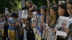 Menschen halten Porträts ihrer vermissten oder gefangenen Verwandten und Freunde in den Händen, während sie in der Region Tschernihiw auf die Ankunft freigelassener ukrainischer Kriegsgefangener warten. (Bild: AFP/GENYA SAVILOV)