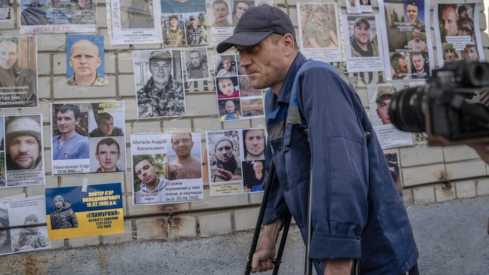 Ein Kriegsgefangener geht an Porträts vermisster oder gefangener Soldaten vorbei.