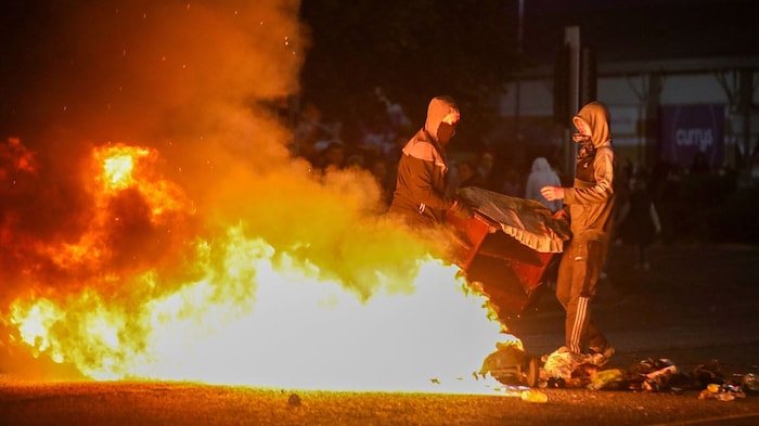 Maskierte Demonstranten werfen Gegenstände auf die Straße.