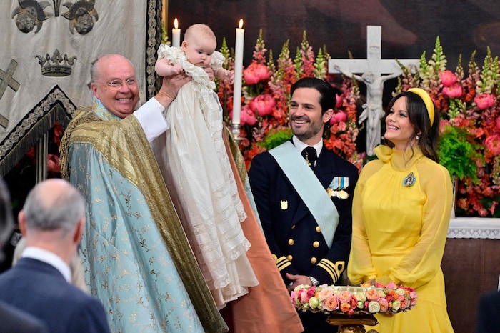 Die kleine Prinzessin bleibt cool, als der Bischof sie hochhebt und der Taufgemeinde ...