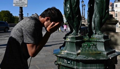 Ein Mann erfrischt sich bei einem öffentlichen Brunnen in Paris.
