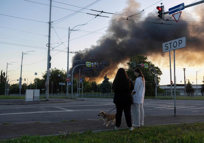 Frauen führen in Kiew den Hund Gassi, während infolge russischer Luftschläge Rauch aufsteigt.