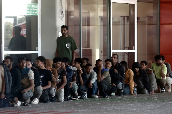 Menschen sitzen vor der griechischen Hafenbehörde.