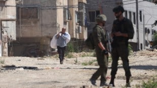 Zwei israelische Soldaten beobachten einen palästinensischen Mann, der mit seinem Hab und Gut ...