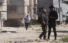 Zwei israelische Soldaten beobachten einen palästinensischen Mann, der mit seinem Hab und Gut ...