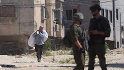 Zwei israelische Soldaten beobachten einen palästinensischen Mann, der mit seinem Hab und Gut ...