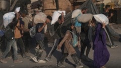 Palästinenser tragen Säcke mit Mehl, die aus einem humanitären Hilfskonvoi entladen wurden,
