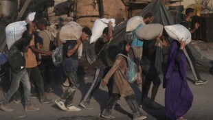 Palästinenser tragen Säcke mit Mehl, die aus einem humanitären Hilfskonvoi entladen wurden,
