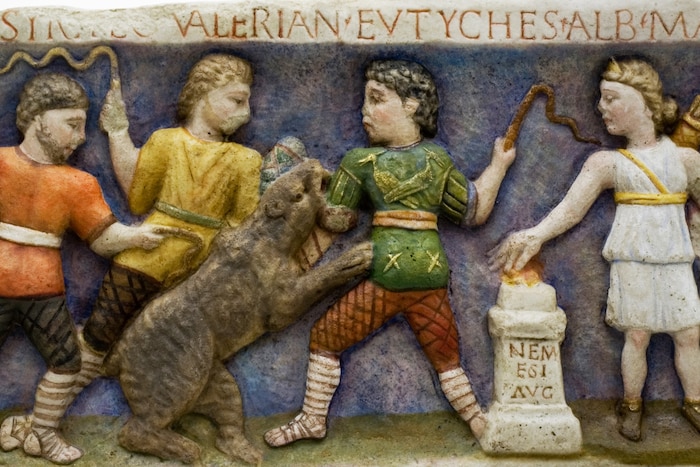 Schicksalsgöttin Nemesis im weißen Chiton und Venatores, die gegen einen Bären kämpfen.