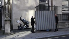 Arbeiter bringen eine Abdeckung an einem Kunstwerk von Banksy an. 