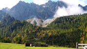 Wundervolle Felswände und Gipfel mit orange verfärbten Bäumen ragen hinter der Eppzirler Alm ...