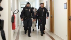 Drei Angeklagte werden schwer bewacht aus der U-Haft vorgeführt.