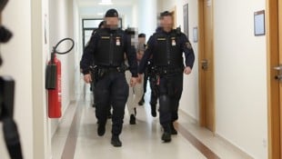 Drei Angeklagte werden schwer bewacht aus der U-Haft vorgeführt.
