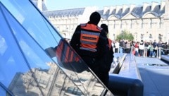 Sicherheitspersonal beobachten die Schlange von wartenden Menschen vor dem Louvre.