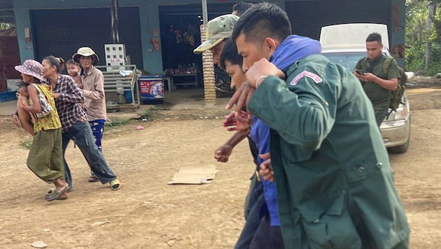Ein verletzter kambodschanischer Mann (2. von rechts) wird von zwei Personen getragen.