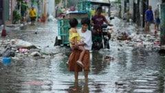 Eine Frau und ein Kind versuchen verzweifelt, eine überflutete Straße zu überqueren.