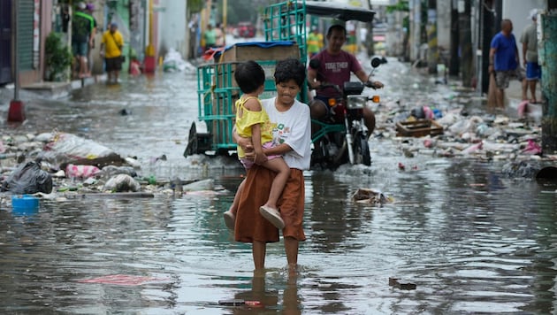 Eine Frau und ein Kind versuchen verzweifelt, eine überflutete Straße zu überqueren.