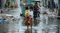 Eine Frau und ein Kind versuchen verzweifelt, eine überflutete Straße zu überqueren.