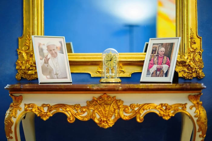 In seinem Arbeitszimmer stehen gerahmte Fotos von Papst Franziskus und Papst Leo.