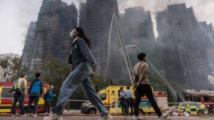 In Grünanlagen und auf Gehwegen rund um die Wohnsiedlung stehen zahlreiche Menschen und starren ...