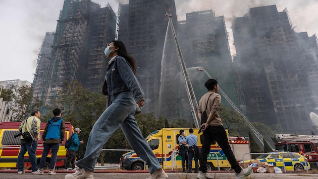 In Grünanlagen und auf Gehwegen rund um die Wohnsiedlung stehen zahlreiche Menschen und starren ...