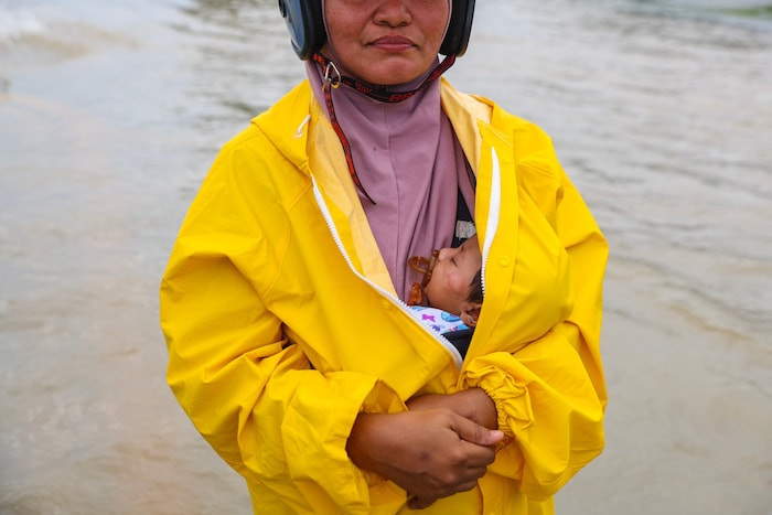 Eine Frau in Malaysia trägt ein Baby, während sie durch das Wasser watet.