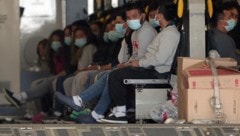 Migranten mit Gesichtsmasken und Fesseln an Händen und Füßen warten in einem Militärflugzeug in ...