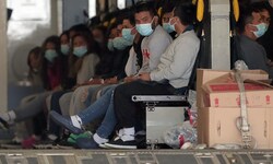 Migranten mit Gesichtsmasken und Fesseln an Händen und Füßen warten in einem Militärflugzeug in ...