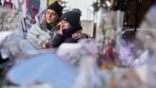 Vor dem ausgebrannten Gebäude legen Menschen still Erinnerungen nieder. Die Trauer ist greifbar.