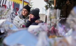 Vor dem ausgebrannten Gebäude legen Menschen still Erinnerungen nieder. Die Trauer ist greifbar.