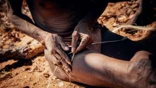 Ein Seilmacher in Namibia beim Herstellen einer Bogensehne. Dabei werden Pflanzenfasern oder ...