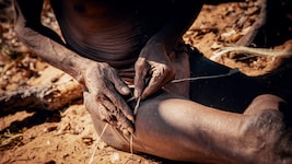 Ein Seilmacher in Namibia beim Herstellen einer Bogensehne. Dabei werden Pflanzenfasern oder ...