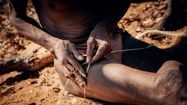 Ein Seilmacher in Namibia beim Herstellen einer Bogensehne. Dabei werden Pflanzenfasern oder ...