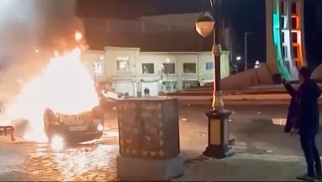 This image was broadcast on Iranian television: a man documents burning vehicles.