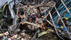 Rettungskräfte mit Schutzhelmen und Bagger suchen in dem Müllberg nach wie vor verzweifelt nach ...